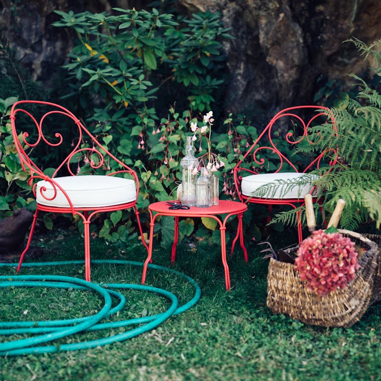 Fermob 1900 French cabriolet iron outdoor armchairs and side table in a garden
