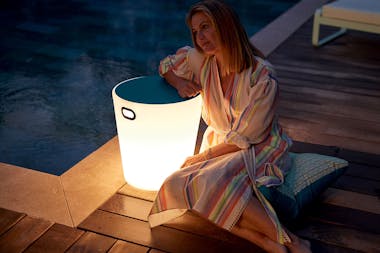 Woman leaning on a lighted stool by pool in the evening