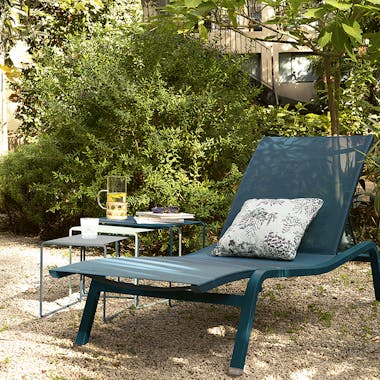 Sunlounger and side tables in blue on gravel in a garden