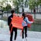 Bright coloured aluminium chairs being carried by a woman and a man by a Paris river