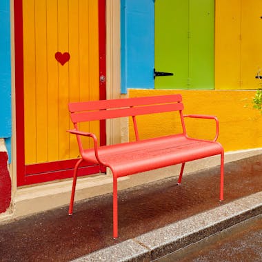 Red bench with arms in front of colourful building
