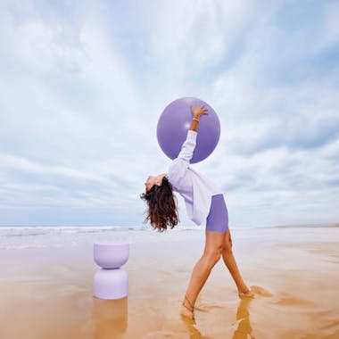 Woman on beach with lavender coloured ball and stool