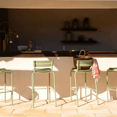 Fermob Luxembourg bar stools in the Cactus colour lined up in the sun in front of a bar