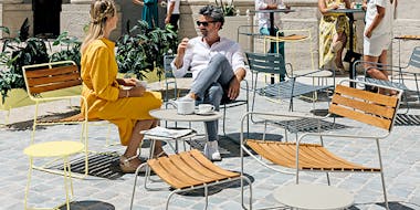 Group of people lounging on Fermob metal outdoor furniture in Frosted Lemon, Clay Grey, and Storm Grey colours
