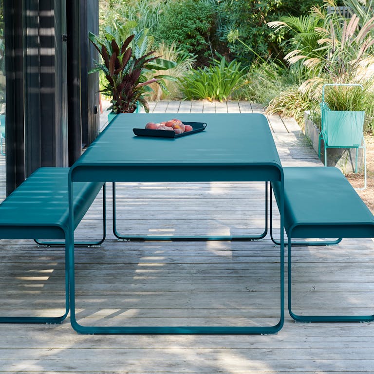 Fermob Bellevie outdoor dining table and benches in Acapulco Blue colour sitting on decking