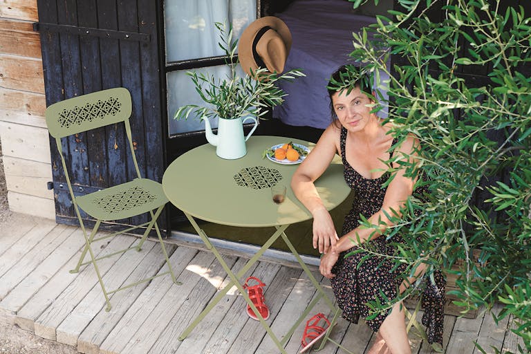 Woman sits at round cafe setting by olive tree