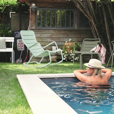 Fermob Luxembourg rocking chair sits on grass behind woman in pool