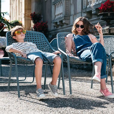 Fermob Croisette outdoor armchairs in storm grey by a chateau with kids