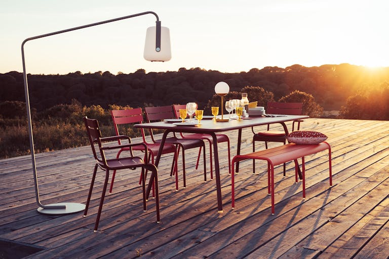 Fermob Luxembourg 8 place outdoor dining setting with bench at sunset under Fermob Balad outdoor lamp on a stand