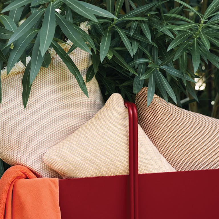 A pile of Fermob Evasion outdoor cushions in a Fermob basket planter