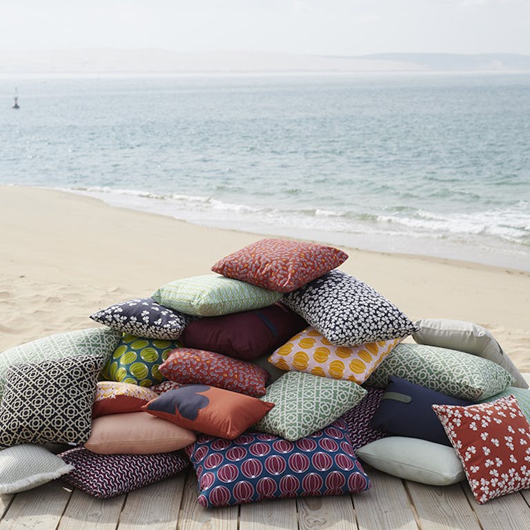 A pile of Fermob outdoor cushions by the beach.