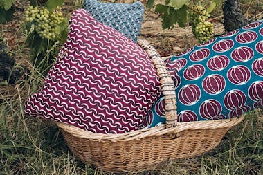 A basket of Fermob Envie d'ailleurs outdoor cushions under a grapevine