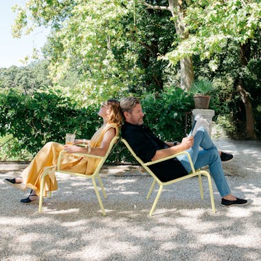 A couple relax outdoors on Fermobs Luxembourg armchairs