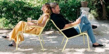A couple relax outdoors on Fermobs Luxembourg armchairs