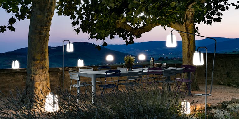 Fermob Ribambelle extending outdoor table in Storm Grey colour sits outside at dusk with 12 seats