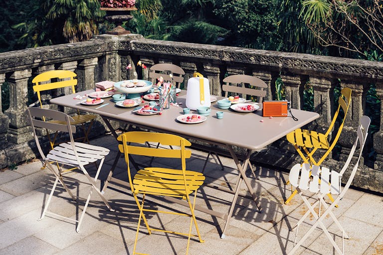Fermob La Mome folding chairs and Caractere large folding outdoor table on a paved terrace