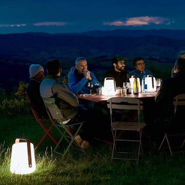 Friends gathered together around Fermob Caractere table with Balad lamps in the evening