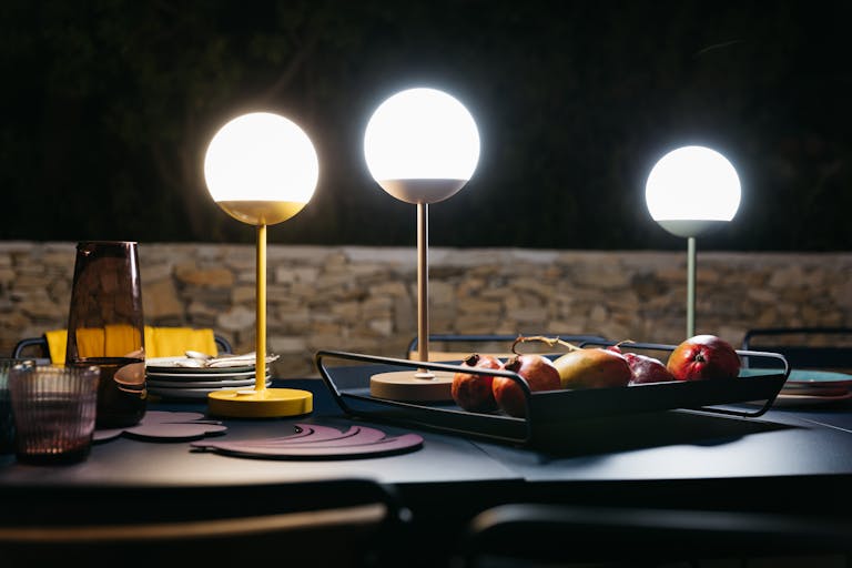 Three Fermob Mooon! LED outdoor lamps light a dining table at night