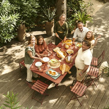 Family gathered together around Fermob Caractere table with Bistro chairs and Luxembourg bench in Red Ochre
