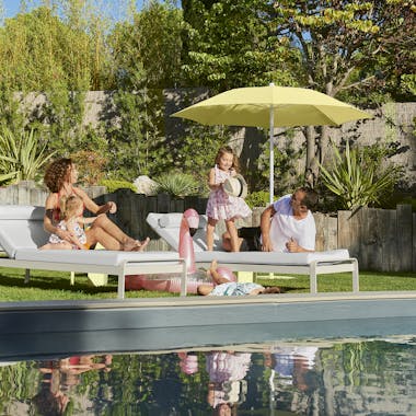Family relaxing on Fermob Bellevie sunlounger with Shadoo parasol in Frosted Lemon