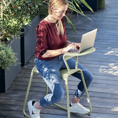 Woman sitting on the Adadesk from Fermob working on her laptop outdoors