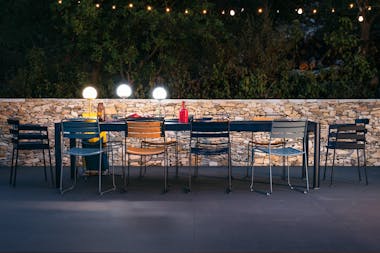Fermob Ribambelle extending outdoor table looking festive at night in front of stone wall